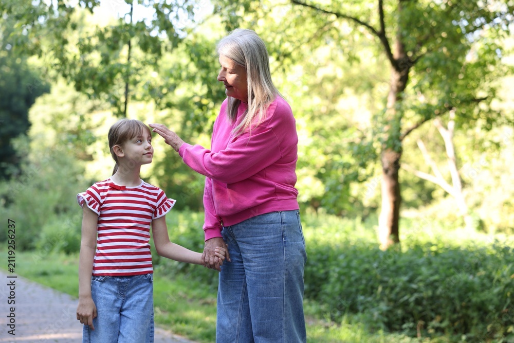 Fototapeta premium Grandmother and granddaughter holding hands while walking in summer park. Space for text