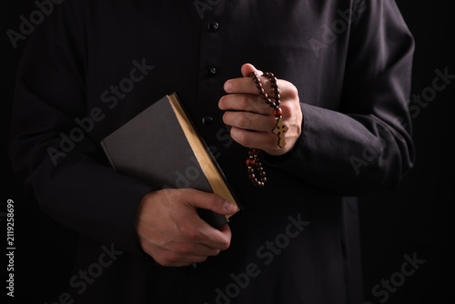 Konstfotografi Priest with rosary and Holy Bible on black background, closeup