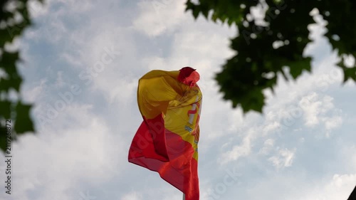Spanish flag waving on a pole against a cloudy sky
