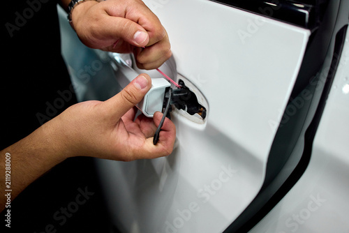 Hands inserting fuel cap into car filler opening beside tethered cap on glossy white body with metal hinge and rubber seal during routine refueling task, with hand, fuel, cap, filler detail