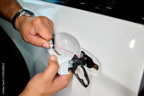Hands inserting fuel cap into car filler opening beside tethered cap on glossy white body with metal hinge and rubber seal during routine refueling task, with hand, fuel, cap, filler detail