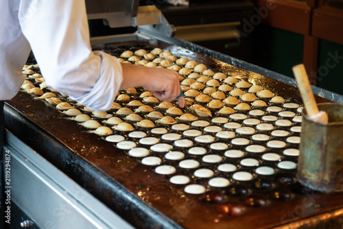 Close-up of a cook flipping traditional Dutch poffertjes on a hot copper or cast-iron plate.