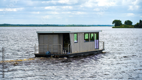 Canvas Print Modern wooden houseboat cruising on a calm lake with water wake