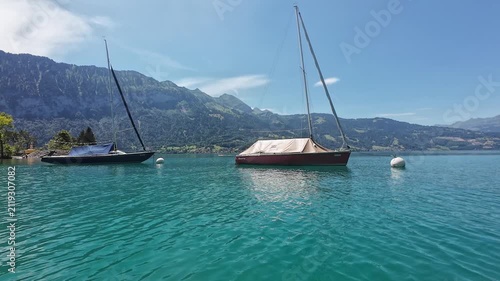 Sailboats anchored on turquoise Thunersee with Swiss mountain backdrop under clear bright summer sky