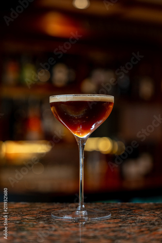 View of an espresso martini cocktail served in a stemmed glass on a polished bar counter in a dimly lit bar in Asker, Akershus, Norway.