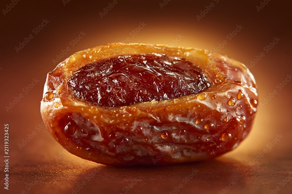 Obraz premium Macro of fresh date cut open showing interior, water droplets, dark brown background with amber glow, soft warm light, sweet fruit photography