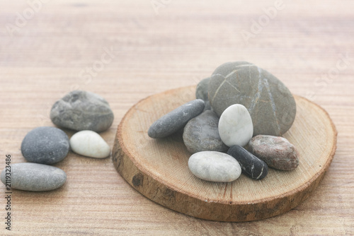 Photography Natural sea pebbles pile on round wooden slice background.