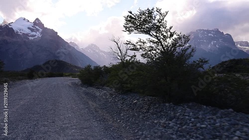 A dynamic clip filmed from inside a car—which does not appear in the video—showing Los Glaciares National Park surrounded by snow-capped mountains; the footage follows a gravel road.