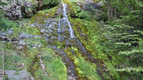 In a slow-motion clip capturing a narrow waterfall from below, it becomes evident that the water appears to gain volume toward the bottom and originates from the middle of a forest.