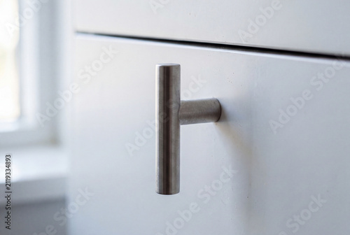 Minimal brushed metal cabinet handle on a white drawer in soft daylight