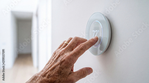 Senior hand adjusts a smart wall thermostat in a bright hallway