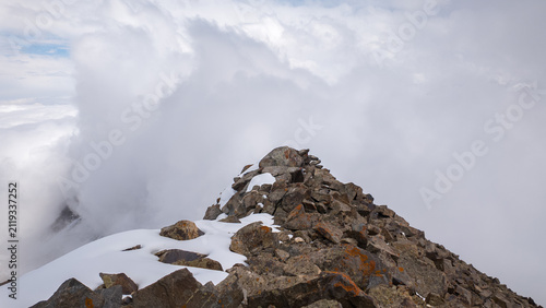 Clouds roll over rugged cliffs and rocky slopes in the breathtaking Pamir Mountains of Kyrgyzstan. Adventurers can explore this stunning gorge through mountaineering and hiking.