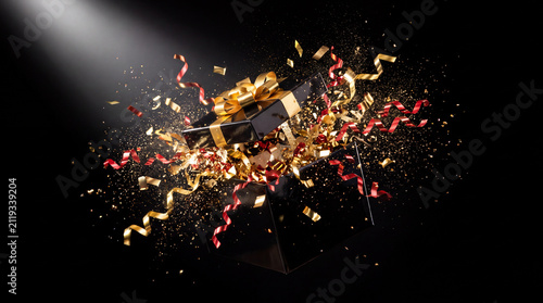 Luxury black gift box bursts open with gold and red ribbon confetti
