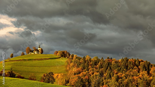 Quadro su tela Sorrowful Mother of God church (Cerkev Zalostne Matere Bozje) on a hilltop, lit by the sun in an otherwise cloudy autumn dawn