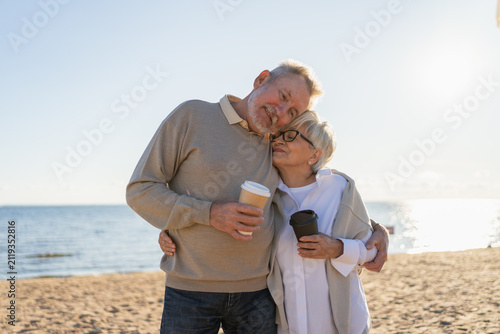 Good morning. Senior mature couple enjoying walking with paper cups of coffee. Old husband wife drinking coffee to go outdoor. Grandmother grandfather together enjoying walk. Family moment of love