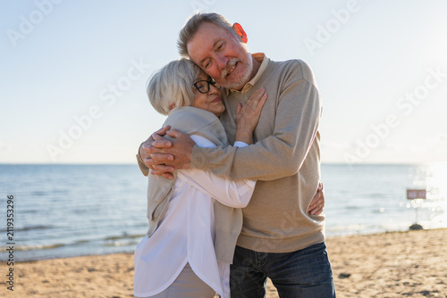 Senior mature couple hugging enjoying outdoor recreation walking on beach. Old husband wife embracing with tenderness love enjoying sweet bonding. Grandmother grandfather together. Family moment love