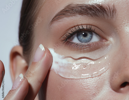 Macro view of a woman applying moisturizing gel cream under her blue eye