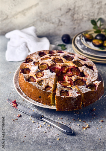 Sliced homemade plum cake on a ceramic plate with vintage knife and fresh fruits, rustic food photography