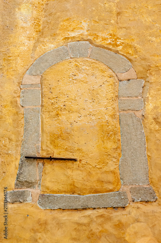 Front view, medium distance of, a 13 century external window, closed with concrete, to become part of a protective wall, under mid-afternoon sunlight