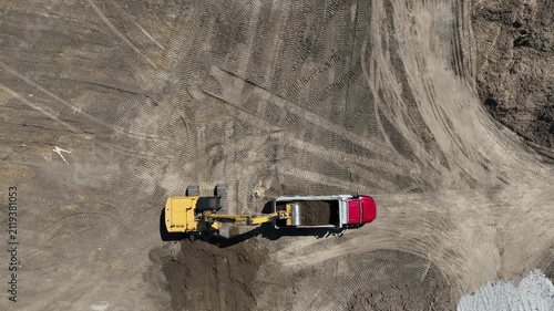 Aerial drone view of a tracked hydraulic excavator loading soil into a dump truck at a construction site before the truck departs, showcasing earthmoving and excavation operations.