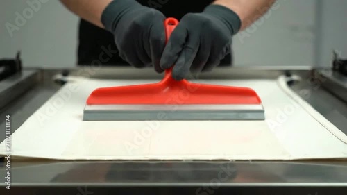 Professional Culinary Technique: Worker Using Red Squeegee to Smooth Dough on Stainless Steel Countertop in Modern Kitchen