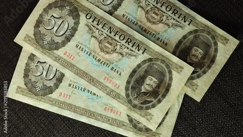 Top view of crisp 1986 Hungarian 50 forint banknotes with consecutive serial numbers falling onto dark brown surface 