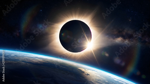 Dramatic solar eclipse over planet Earth with sun flares and rainbow halo.