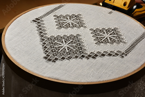 A close-up of traditional drawn thread embroidery in progress on natural linen fabric stretched in a wooden embroidery hoop.