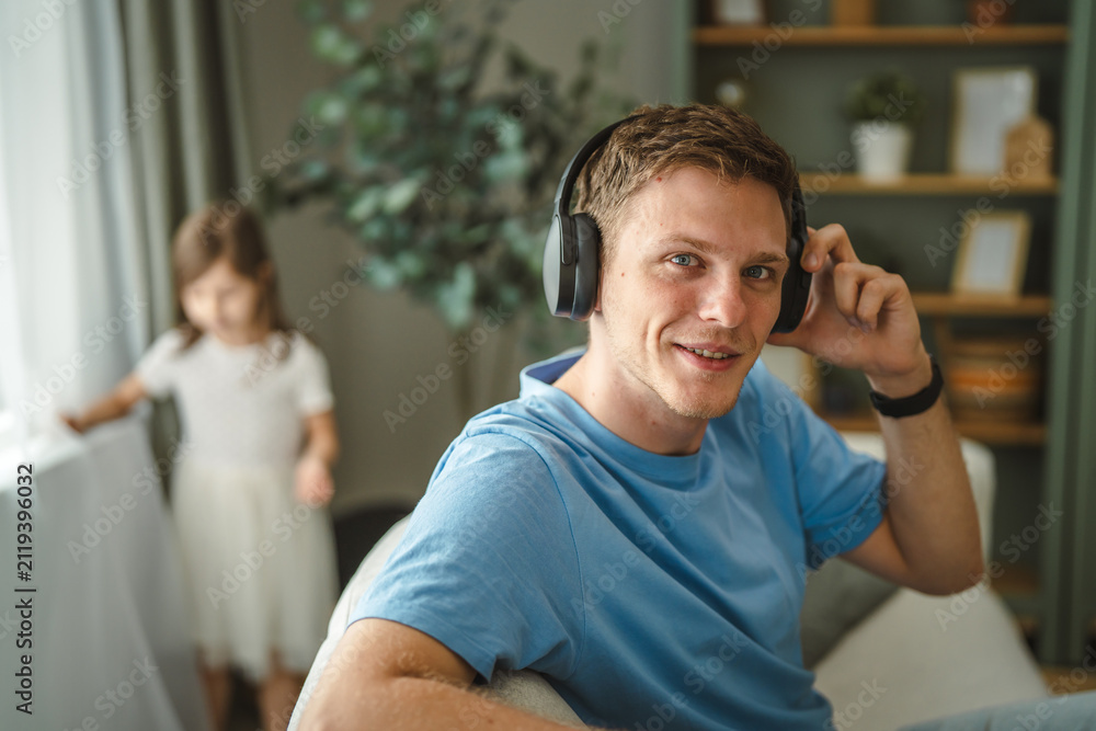 Fototapeta premium Father enjoying music with headphones while daughter playing at home