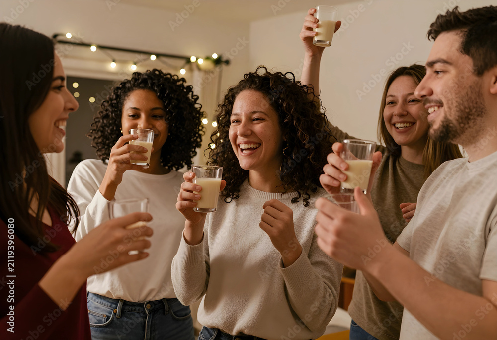 Obraz premium Diverse group of happy young adults toasting with glasses of eggnog at a festive holiday gathering, Friends are smiling and laughing while enjoying drinks together in a warm, cozy indoor setting