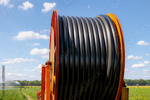 Sumer countryside landscape, Large industrial hose reel irrigator watering a crop field under blue sky with white cloud, Farming irrigation technology system spraying water, Agriculture in Netherlands
