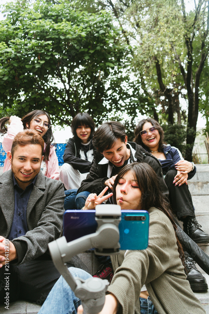 Fototapeta premium Group of cheerful Hispanic university friends laughing and posing for a vlog with a smartphone on a gimbal