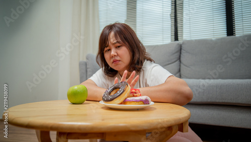 Overweight teenage girl rejecting sweets and choosing fruit for healthy eating, weight loss, obesity prevention, nutrition, and wellness concept.