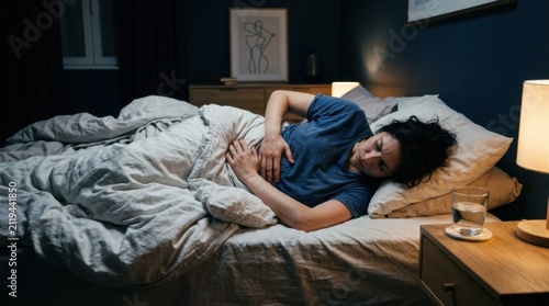 Woman In Bed Feeling Unwell At Night With Stomach Pain