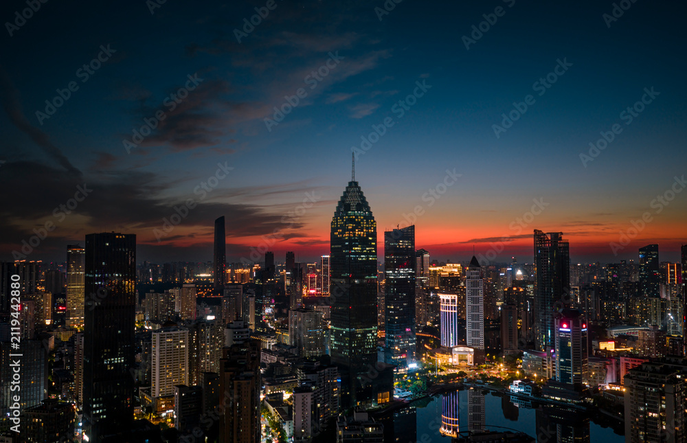 Obraz premium Aerial twilight view of Wuhan Financial Street CBD. The towering, illuminated skyscrapers reflecting in the water symbolize the dynamic growth of China's economy.