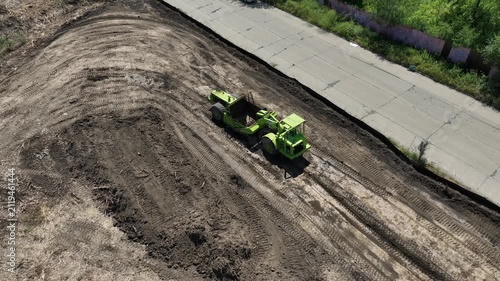 Self-propelled earth scraper loading its bowl with soil while grading a construction site, captured from a side aerial drone view during earthmoving operations.
