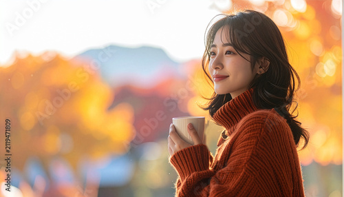 紅葉した綺麗な山並みをバックに温かいマグカップを持ち優しくほほ笑む女性