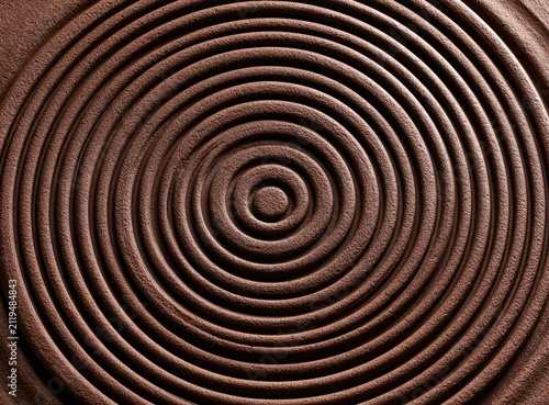 Abstract concentric spiral pattern in rich brown clay with textured ridges