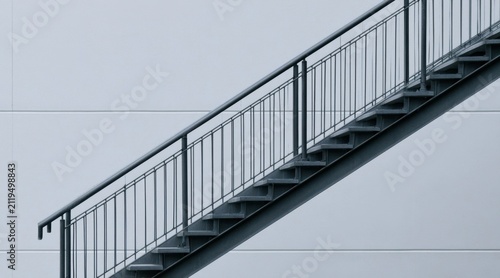 Metal staircase with black railing ascending diagonally against a light gray wall