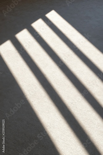 Diagonal light beams on a dark floor creating strong contrast and geometric shadow patterns
