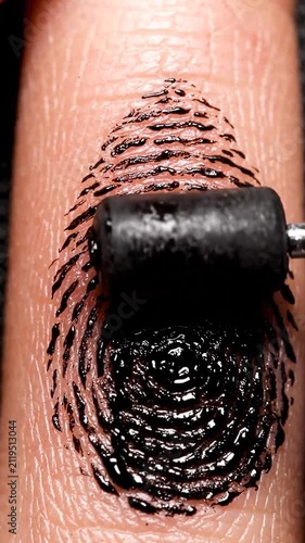 Close-up of Black Ink Being Applied to a Human Finger with a Roller for Biometric Fingerprinting