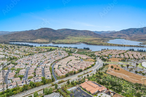 An aerial view of a large housing community near Otay Lakes in Chula Vista featuring dense suburban single-family blocks, winding green parkways, and close proximity to the Lower Otay Lake reservoir