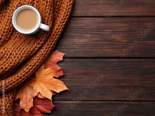 Autumn cozy coffee with a brown scarf and maple leaves on a rustic wooden fall desk
