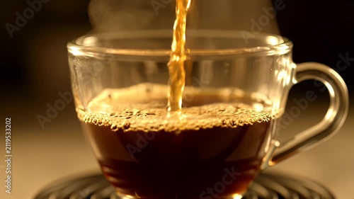 Hot coffee pouring into a clear glass cup with steam rising in warm soft lighting