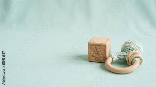 Wooden Alphabet Block and Knitted Baby Rattle on a Soft Pastel Green Background