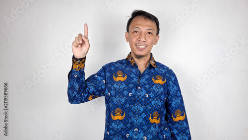 Foto Young male civil servant pointing upward copyspace in blue batik uniform