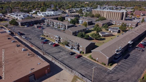 Daytime aerial view of an organized residential neighborhood with multifamily housing complexes, parking, and tree-lined streets.