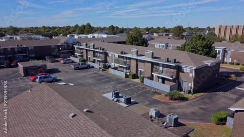 Sunny daytime aerial view of a residential neighborhood with rows of multifamily housing buildings and organized parking.