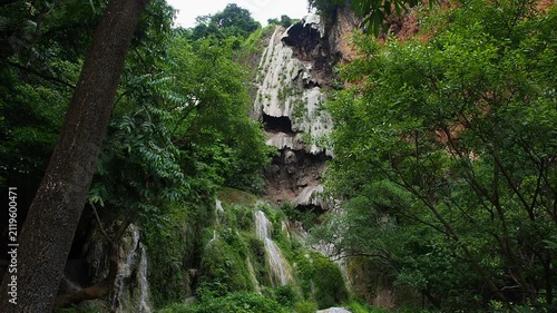 A waterfall with clear blue water, surrounded by natural rock formations and lush trees.