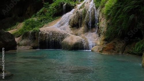 A waterfall with clear blue water, surrounded by natural rock formations and lush trees.